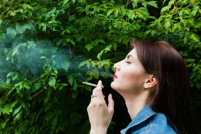 Young woman smoking cigarette by plants