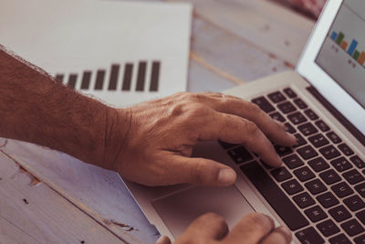 Cropped hand of man working over laptop in office