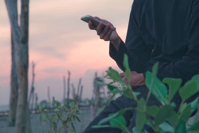 Close-up of man holding smart phone against sky