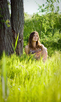 Woman smiling while sitting on grass against trees