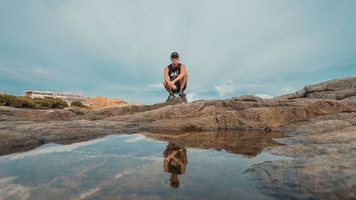 Man standing on rock by sea against sky