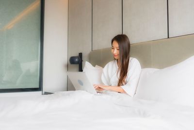 Young woman using mobile phone while sitting on bed