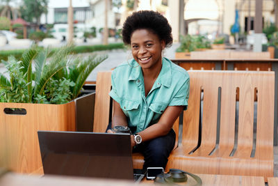 Portrait of smiling young woman using laptop on table at outdoor cafe