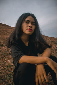 Portrait of young woman sitting on field against sky