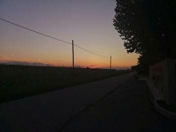 Road by silhouette trees against sky during sunset