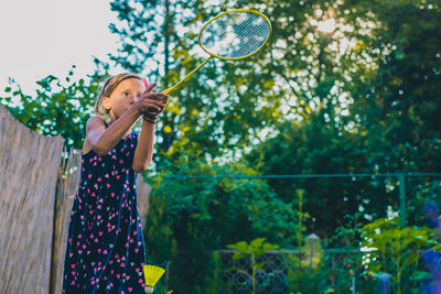 Girl playing badminton while standing by flowering plants