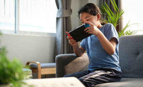 Full length of boy sitting on sofa at home