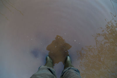 Legs in green rubber boots and green pants standing in dirty brown puddle - first person view