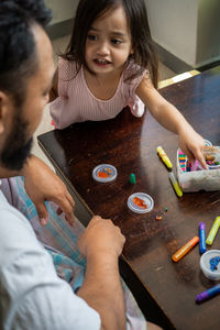 High angle portrait of family painting togeher using glitter glue arts and craft set.