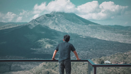 Rear view of man standing on mountain against sky