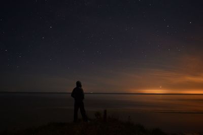 Silhouette mid adult man standing at beach against sky during night