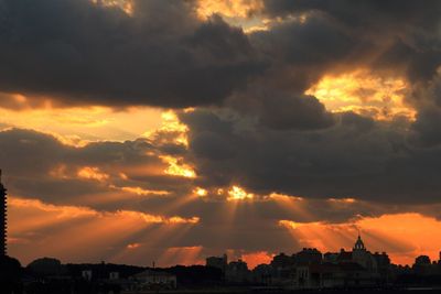 Silhouette of city against cloudy sky during sunset