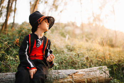 Boy wearing costume during halloween sitting on wood at forest