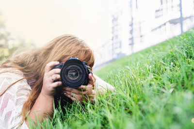 Young woman photographing through camera while lying on grass outdoors