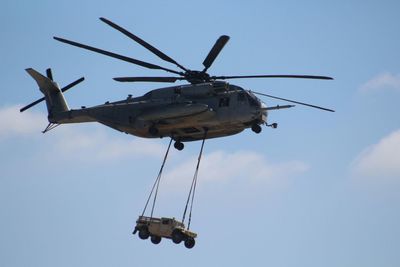 Low angle view of military helicopter carrying jeep against sky