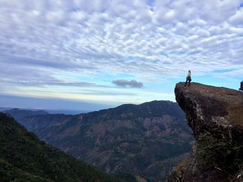 Hiker standing on mountain against cloudy sky