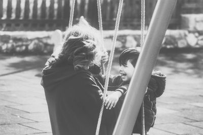 Side view of grandmother with grandson sitting on swing at playground