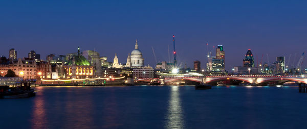Illuminated st paul cathedral amidst buildings by thames river against sky at night