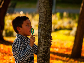 Boy holding magnifying glass by tree