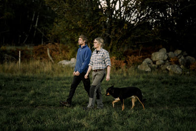 Mature couple walking with dog on field at sunset