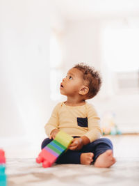 Cute boy looking away while sitting on floor at home