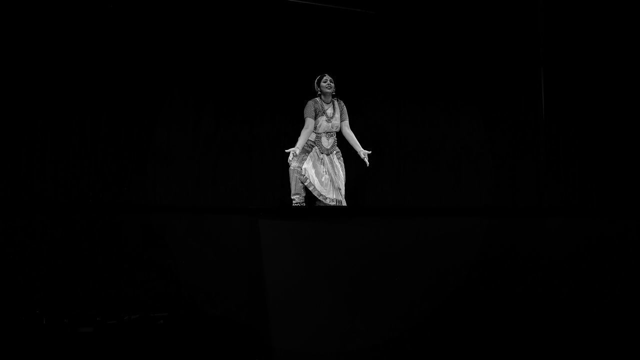 MIDSECTION OF WOMAN STANDING AGAINST DARK BACKGROUND