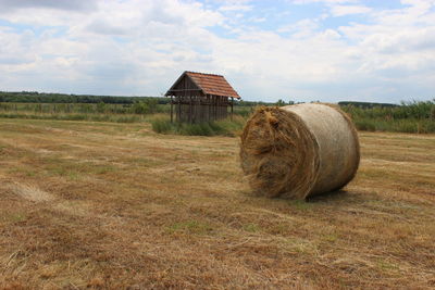 Old hay bales on field against cloudy sky