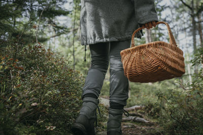 Low section of woman carrying wicker basket while walking by plant