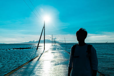 Rear view of man standing at beach against sky