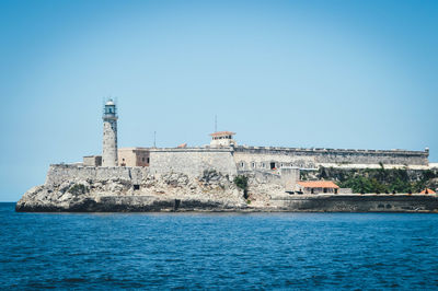 Building by sea against clear blue sky