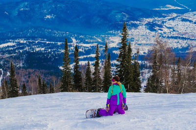Full length of woman kneeling on snow covered land against trees