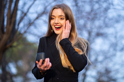 Low angle view of smiling young woman against sky