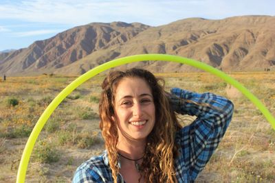 Portrait of smiling young woman with plastic hoop against mountain and sky