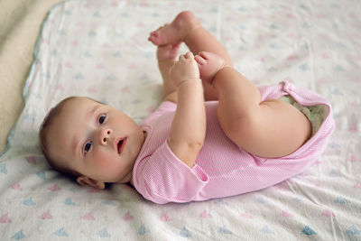 Girl child in pink clothes lying on his back on the bed