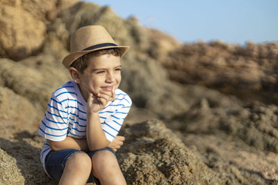 Cute boy wearing hat sitting on rock