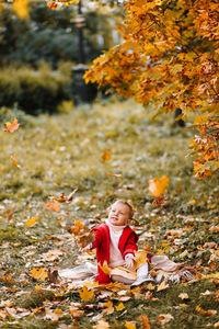 Funny little girl in a red coat catches fall leaves having fun and walking in the autumn forest