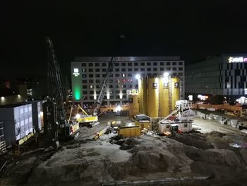Illuminated construction site by buildings in city at night