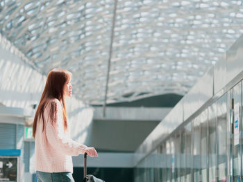  woman in warm suit touch and push on luggage handle with modern train station