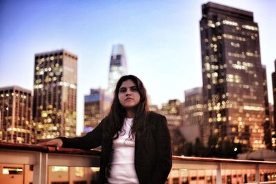 Portrait of young woman standing against illuminated buildings in city