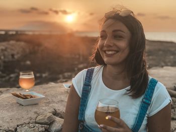 Portrait of smiling young woman holding drink at sunset