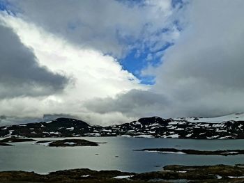 Scenic view of sea by mountain against sky