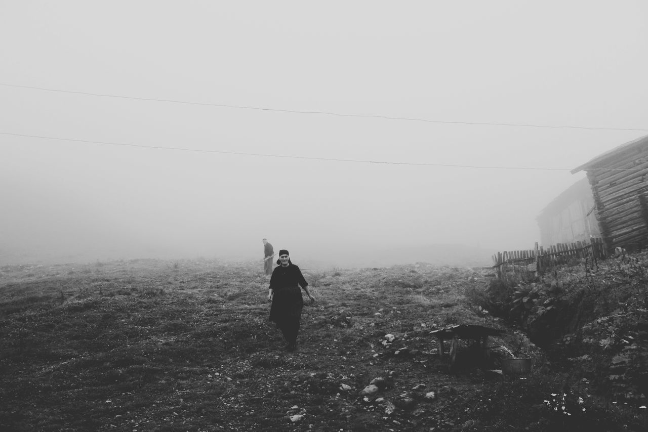 PEOPLE ON FIELD BY ROAD AGAINST SKY