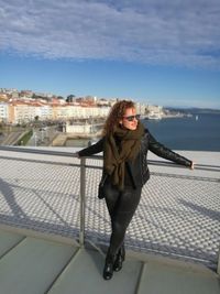 Full length of woman standing by railing against sky in city