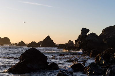 Rock formation on beach against sky during sunset