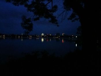Reflection of silhouette trees in calm water at night