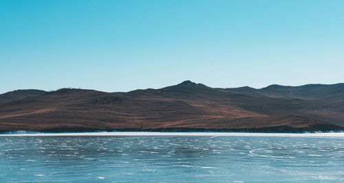 Scenic view of lake by mountains against clear blue sky