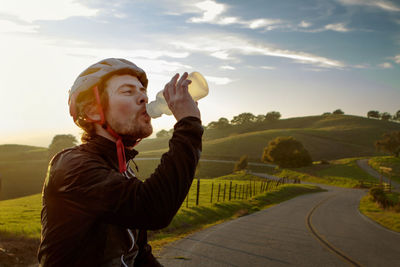 Man wearing helmet while drinking water against sky