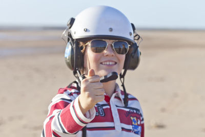 Portrait of young man wearing sunglasses and helmet while standing at beach