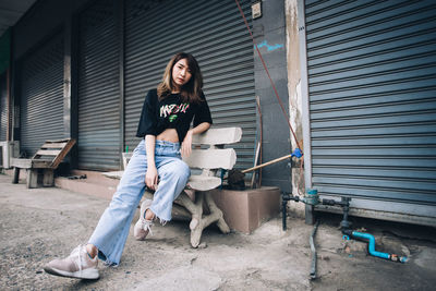 Portrait of young woman sitting on shutter