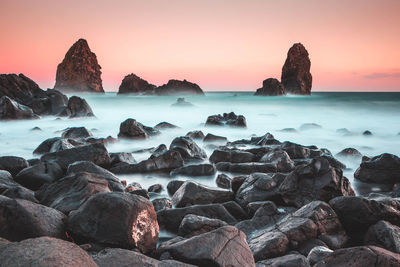 Rocks on beach against sky during sunset